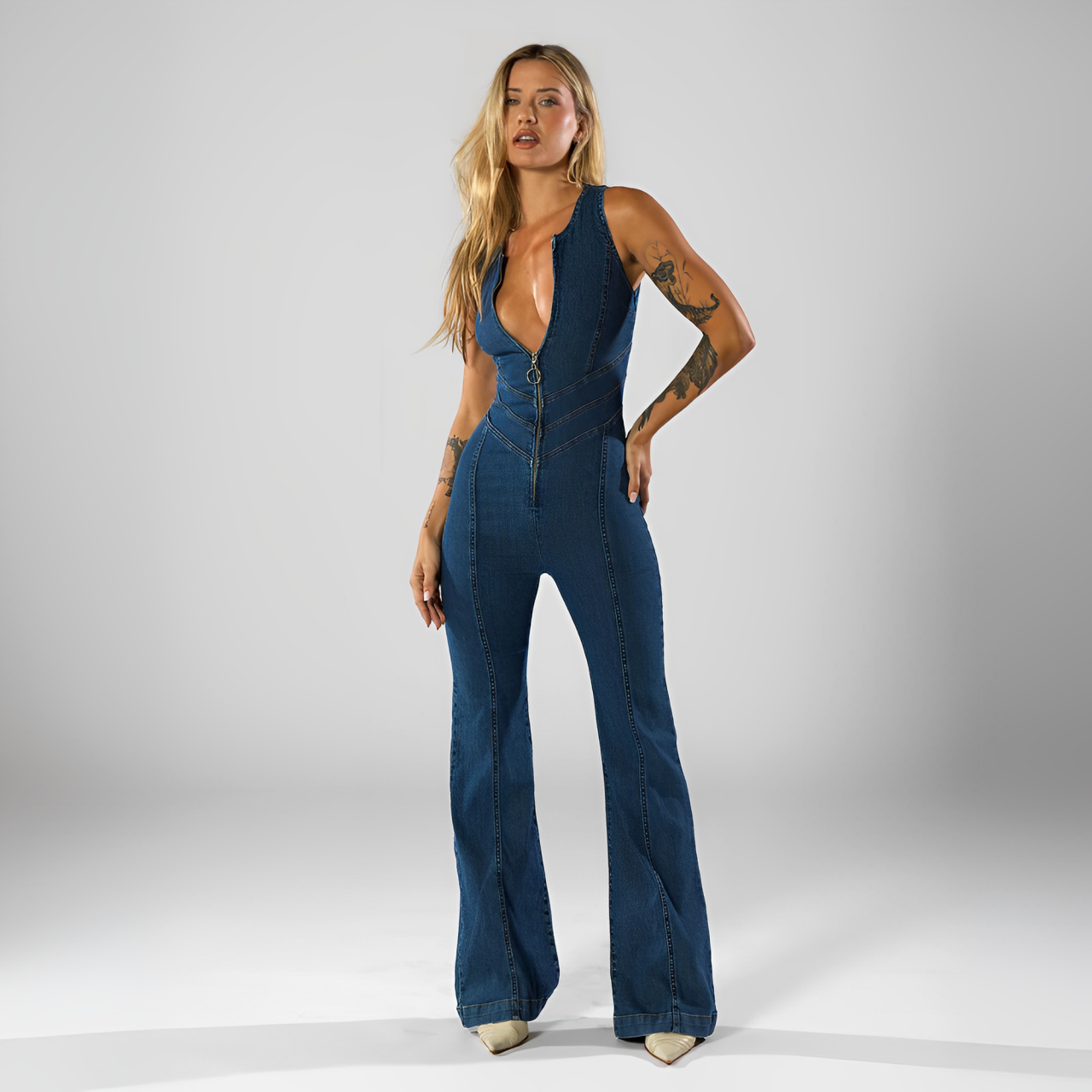A woman standing and wearing a blue backless heart denim jumpsuit.