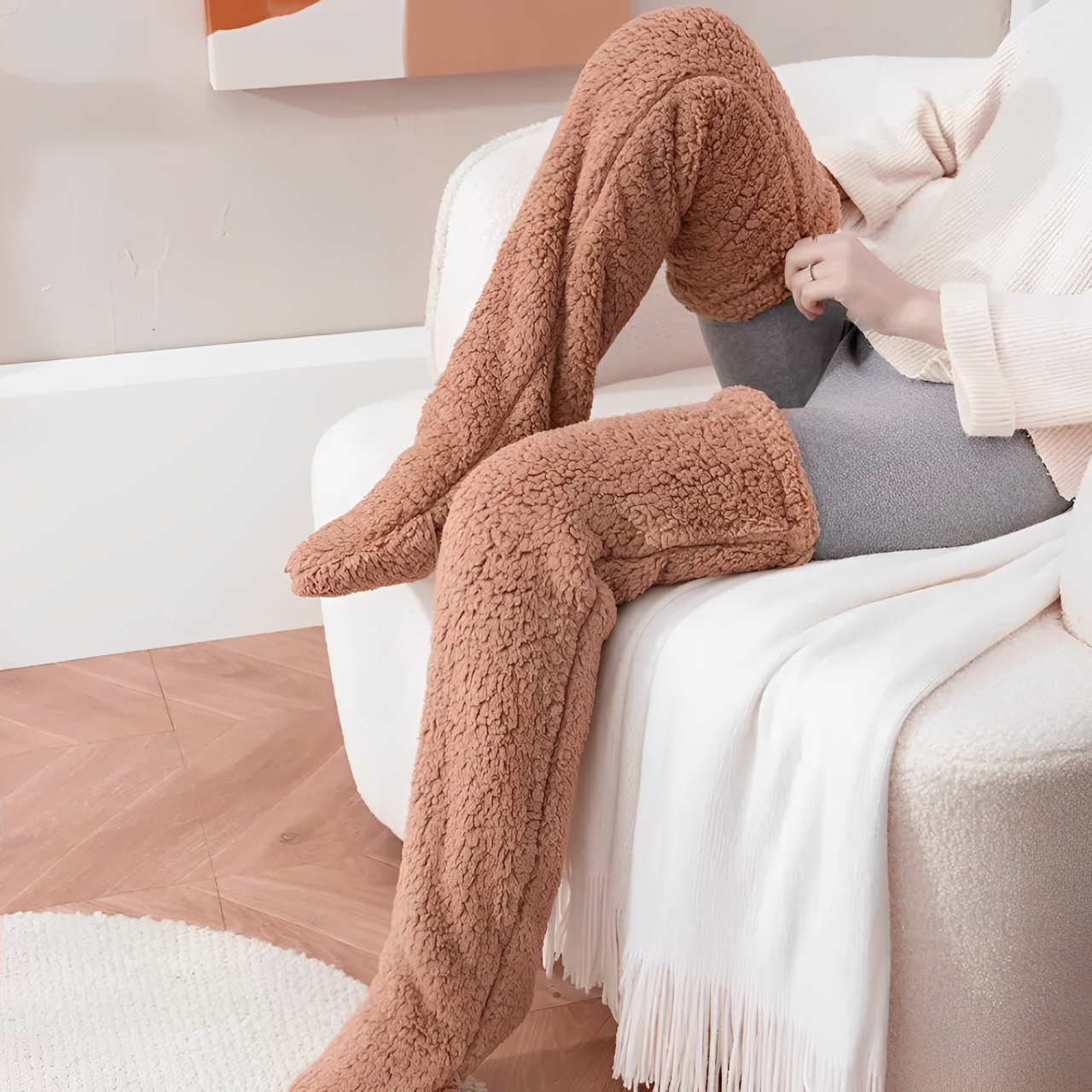 A woman sitting down and putting on brown plush knee high socks.