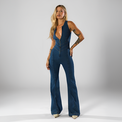 A woman standing and wearing a blue backless heart denim jumpsuit.