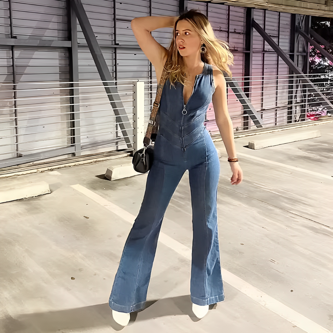 A woman standing in a car park wearing a blue backless heart denim jumpsuit.