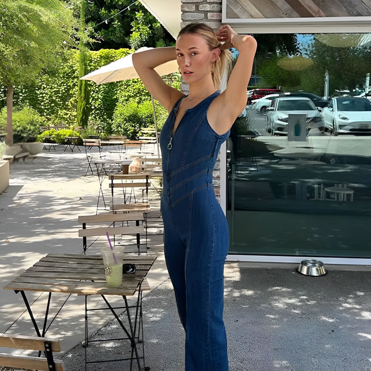 A woman outside a cafe and wearing a blue backless heart denim jumpsuit.