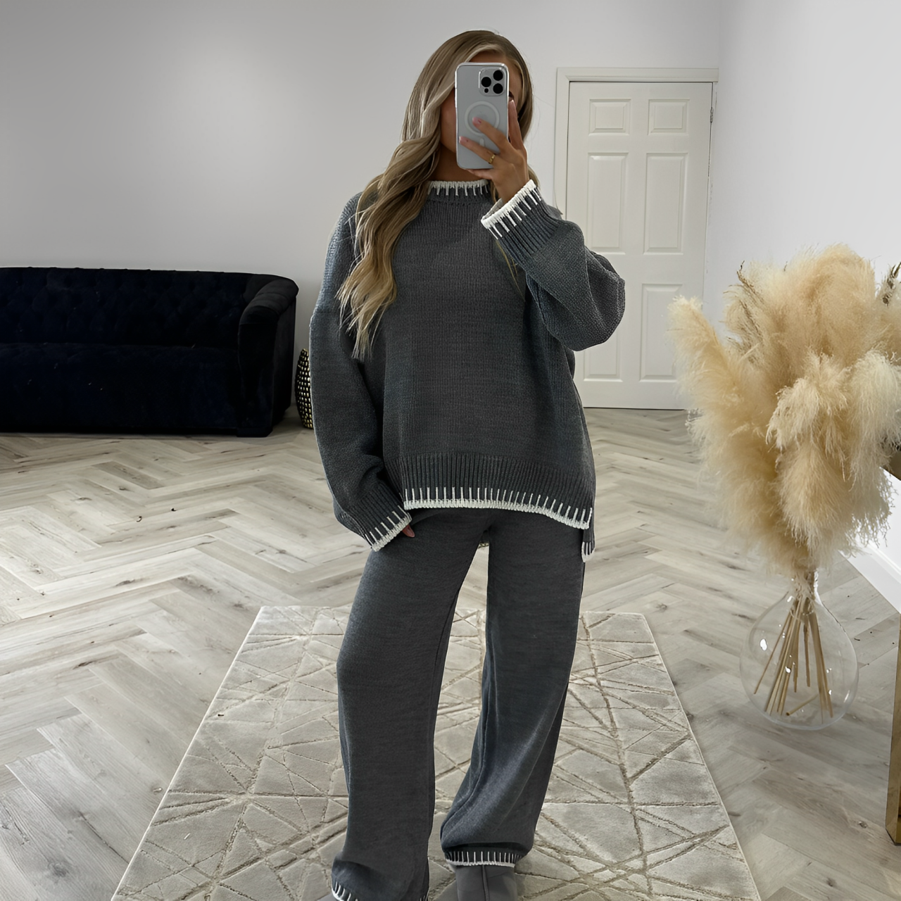 A woman standing in the middle of the room and wearing gray knitted sweater and pants set.