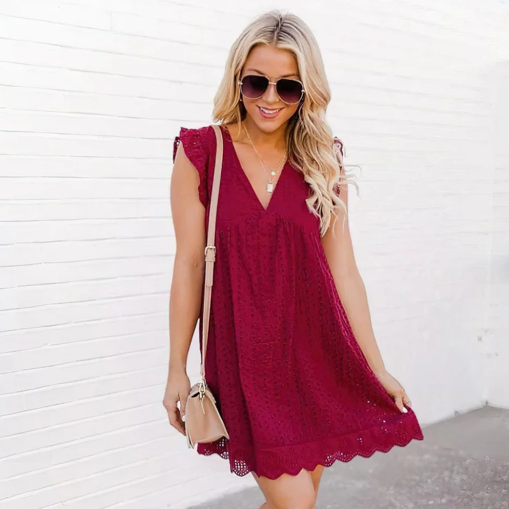 A woman standing in front of a white wall and wearing a red romper pocket dress.