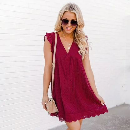 A woman standing in front of a white wall and wearing a red romper pocket dress.